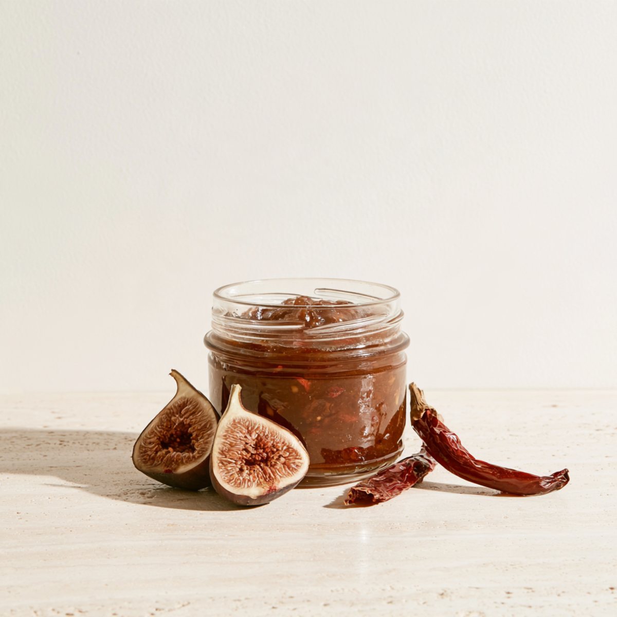 Konfitura z fig z papryczką chili w szklanym słoiku, obok świeże figi i suszona papryczka